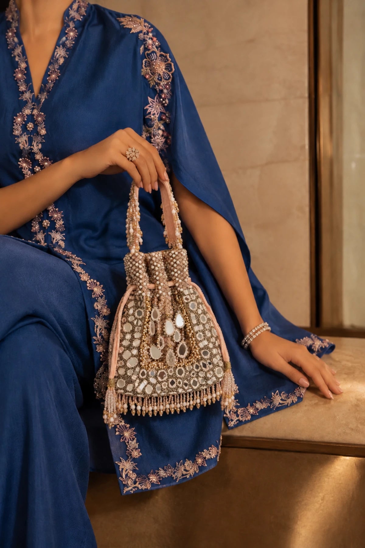 Designer baby pink potli bag with intricate mirror detailing and handcrafted embellishments for festive occasions.